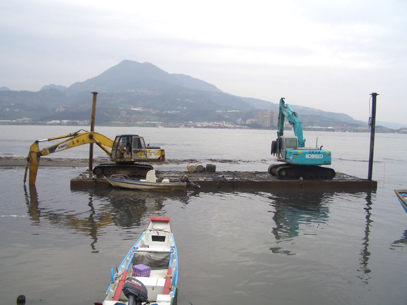 "怪手撐篙". 兩輛挖沙的挖土機(怪手)停在浮台上, 藉著將怪手伸入水底"撐篙", 來移動浮台的位置.